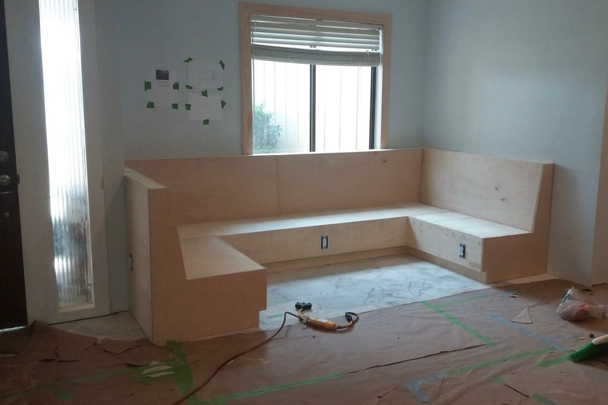 Living room corner with an L-shaped plywood built-in bench seat under a window