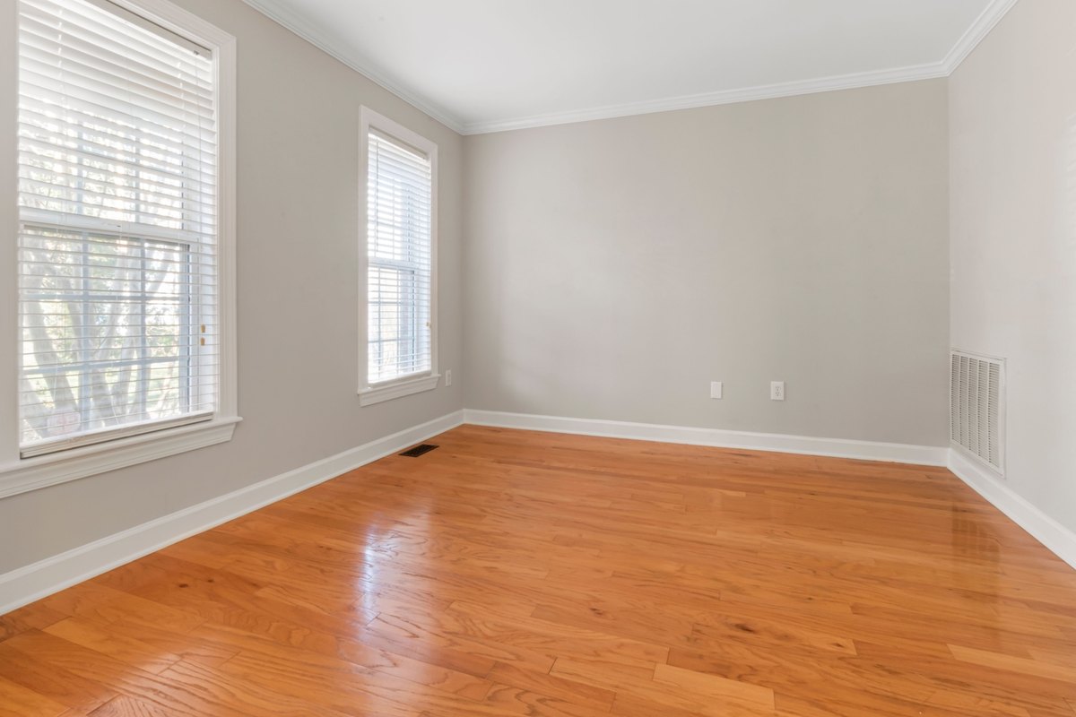 Empty room with a glossy honey-colored hardwood plank floor and white baseboards
