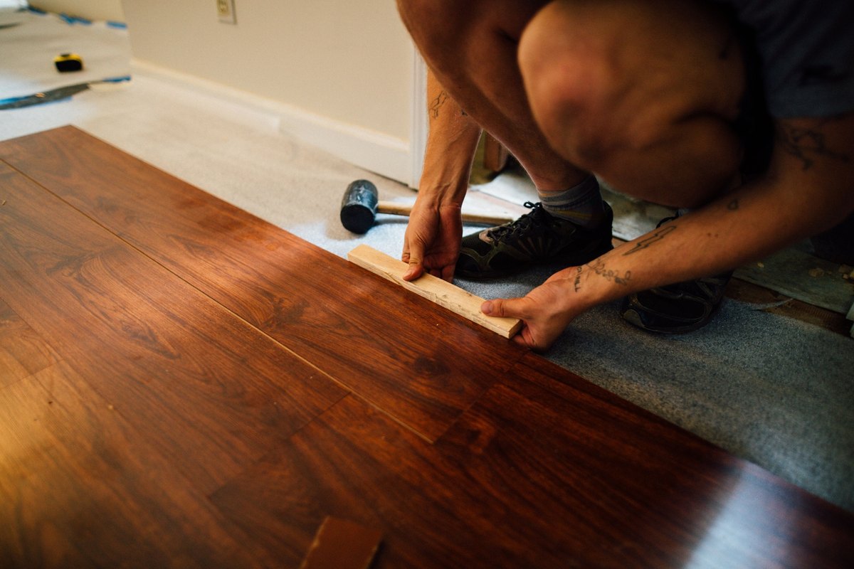 Installer tapping a dark wood-look laminate plank into place with a wood block