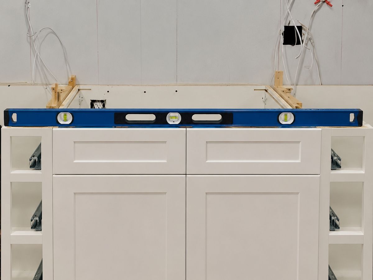 White shaker sink base cabinet flanked by open narrow cabinets showing drawer slides