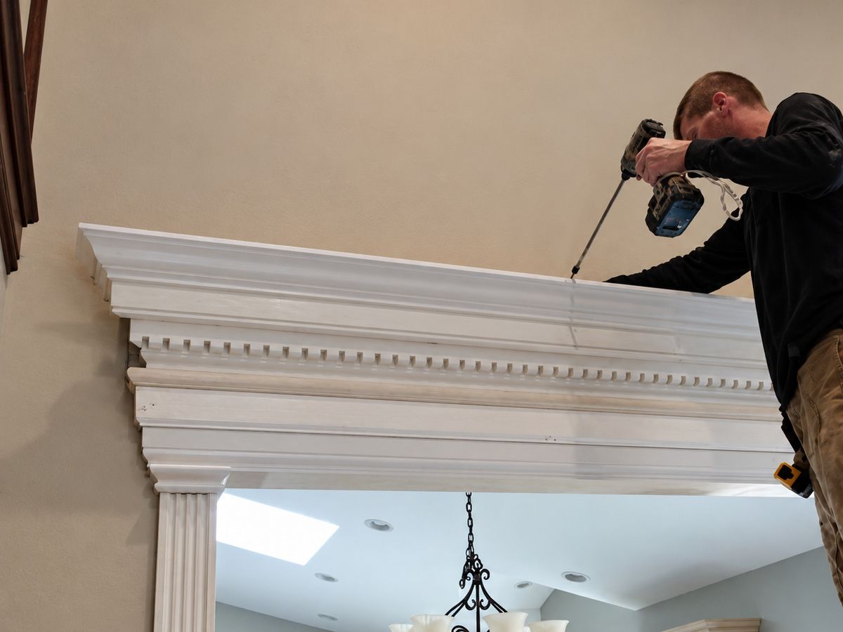 Carpenter leaning over a tall white built-up header with a dentil row above a wide opening