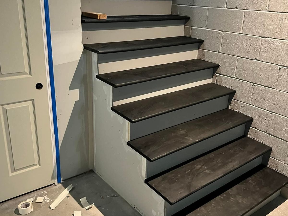Finished basement stairs with white painted risers and dark gray plank treads beside a white paneled door