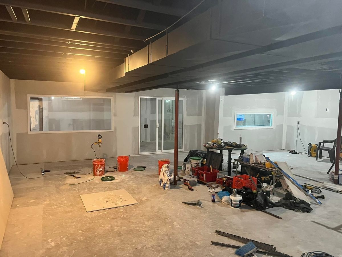 Open basement with drywall walls, a long window in the back wall, and tools on the concrete floor
