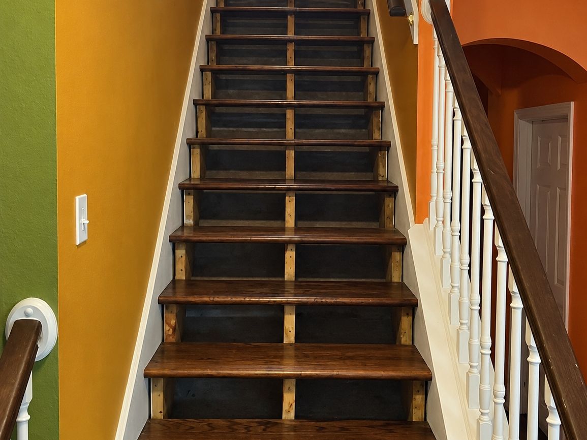 Straight wood staircase with refinished dark treads between orange and green walls and white balusters