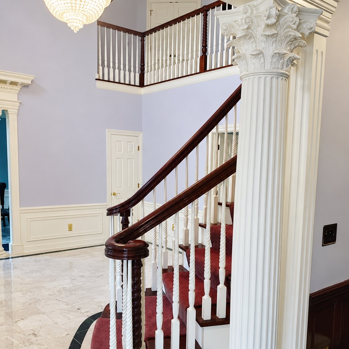 Two-story foyer with a curved mahogany handrail, white wainscoting, and lavender walls