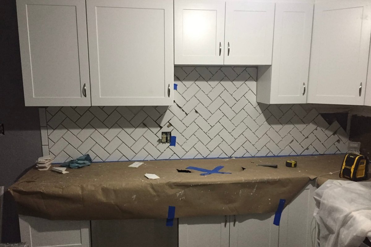 Kitchen with white shaker cabinets and a herringbone white tile backsplash partly set above brown paper