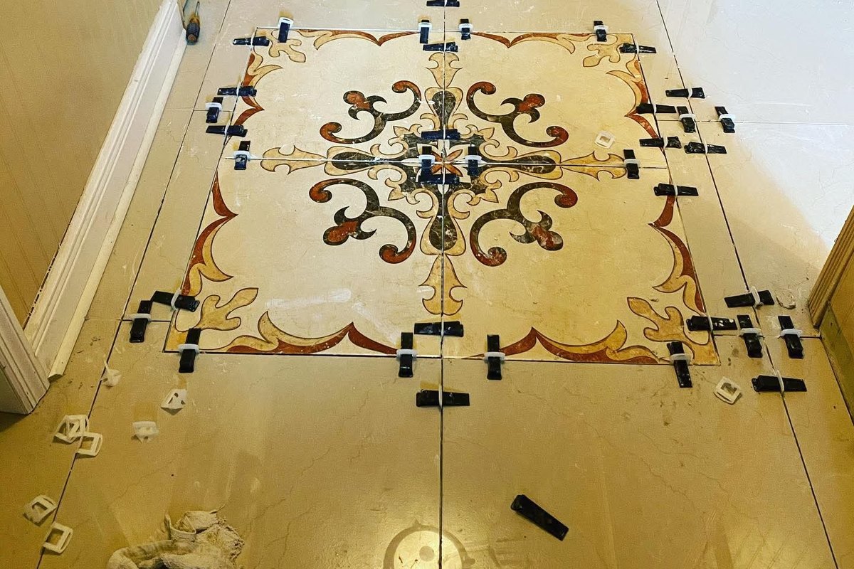 Hallway of large polished cream tiles laid around an inlaid scrollwork medallion with black spacers