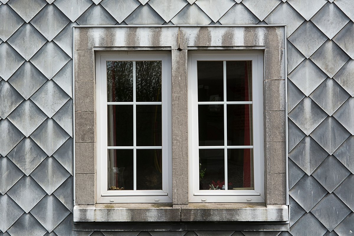 Pair of white six-lite windows in a stone surround on a slate shingle wall